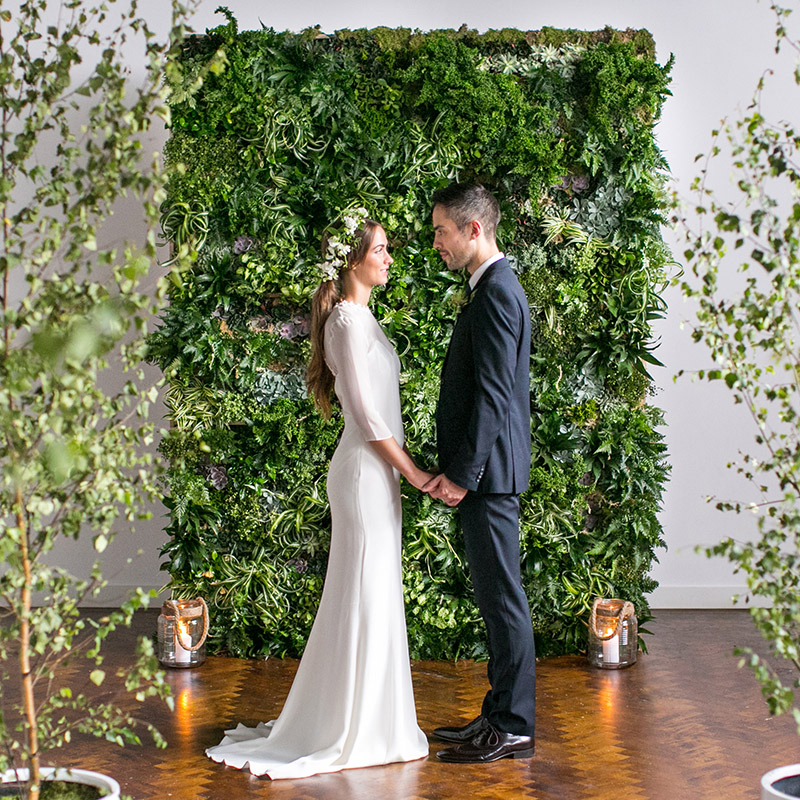 City-chic London wedding venue with a view 2 a man and woman holding hands in front of a wall of plants